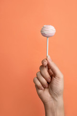 Woman holding sweet cake pop on coral background, closeup