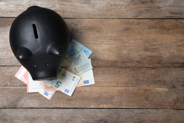 Top view of piggy bank and Euro banknotes on wooden table, space for text. Money savings
