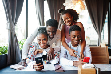 Happy african friends sitting and chatting in cafe. Group of black peoples meeting in restaurant hugs and look at their mobile phone.