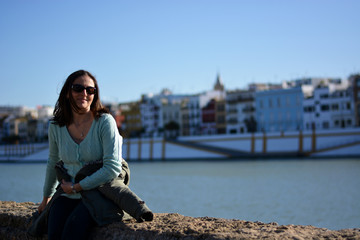 the girl smiles sitting at the edge of the Guadalquivir river, in Seville, Spain