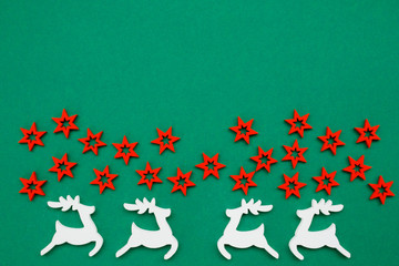 Wooden handmade Christmas decorations white Deers and red Stars with a pattern on a green isolated background. Flat lay, top view with copy space. Merry Christmas and Happy New Year concept.