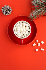 Obraz na płótnie Canvas Hot chocolate with marshmallows in the red cup and Christmas composition on the red background. Top view. Copy space. Location vertical.