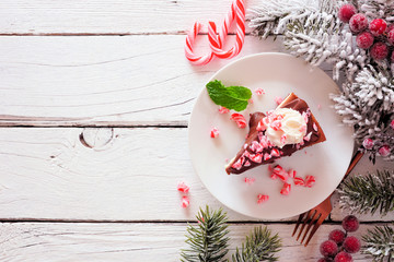 Christmas holiday candy cane chocolate cheesecake. Above view side border over a white wood...
