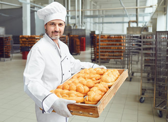 A baker in a bakery against the shelves of bread. - obrazy, fototapety, plakaty