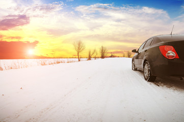 Fototapeta na wymiar Car on the winter countryside road with snow against a sky with a sunset