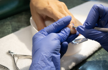 Male manicure. Woman hands in blue sterile gloves holding male finger and manicure instrument making manicure procedure.