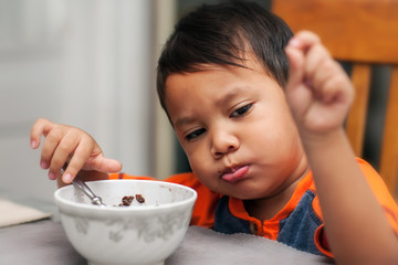 A male child eating his breakfast with a mouthful of food.