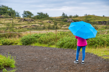 Young girl looking at green park holding blue umbrella, back view