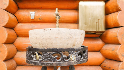A stone washbasin on a metal forged stand in a log house. Interior in a house made of wood.