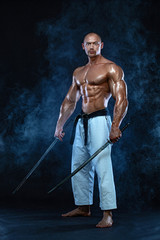 Shirtless man samurai with Japanese sword. Karate fighter on black background with smoke. Handsome...