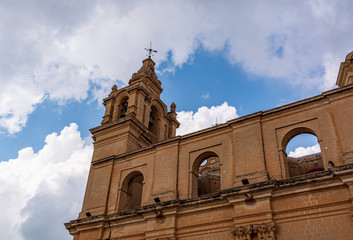 Fototapeta premium St Paul's Cathedral bell tower shot from low angle against blue cloudy sky, in Mdina, Malta.