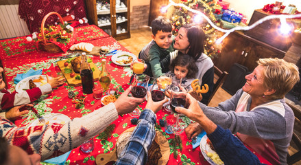 Happy multi generation family having fun at christmas supper party - New year's eve mood with group toasting red wine glasses - Winter holiday concept with parents and children eating together at home