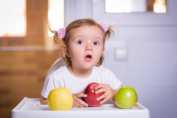Fototapeta premium Cute baby 1,4 years old sitting on high children chair and eating fruit alone in white and brown kitchen