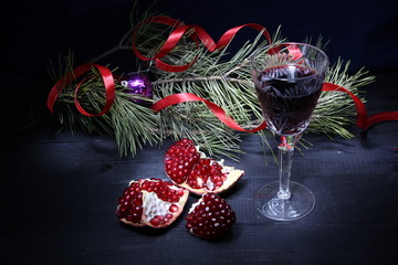 Christmas and new year card with red wine glass, ripe ruby pomegranate,  decorated pine branches on black background