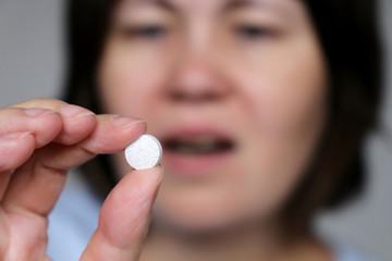 Woman taking pill, girl with open mouth holding white tablet in hand. Concept of medication,...