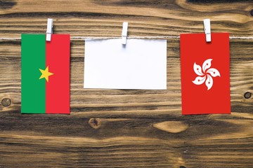 Hanging flags of Burkina Faso and Hong Kong attached to rope with clothes pins with copy space on white note paper on wooden background.Diplomatic relations between countries.