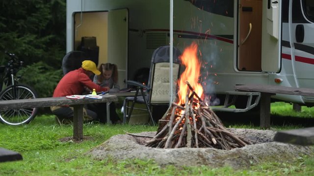 Father Drawing His Daughter on the Camping. RV Camper Van and Camp Fire. Caucasian Family Outdoor Time.