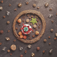 A green fir cone along with red berries is in a white bowl on a green star-shaped plate. Nearby are various decorations (wicker wreath, glass balls, anise, metal stars and dried plants).