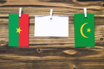 Hanging flags of Burkina Faso and Mauritania attached to rope with clothes pins with copy space on white note paper on wooden background.Diplomatic relations between countries.