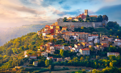 Antique city Motovun Croatia Istria. Picturesque panorama age-old village at hill with pink cloud and sunny light and authentic home with red tegular roof and green vineyard garden. - obrazy, fototapety, plakaty