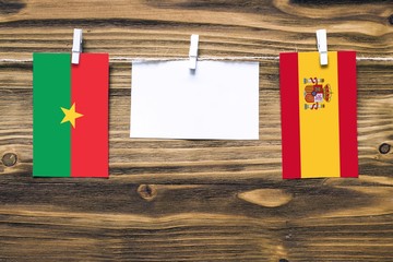 Hanging flags of Burkina Faso and Spain attached to rope with clothes pins with copy space on white note paper on wooden background.Diplomatic relations between countries.