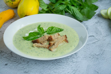 Cream soup made from mashed potatoes with zucchini and basil and crackers on a light background. Space for text.