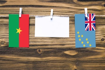 Hanging flags of Burkina Faso and Tuvalu attached to rope with clothes pins with copy space on white note paper on wooden background.Diplomatic relations between countries.