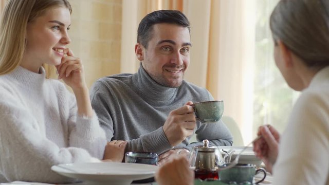 Tracking Medium Shot Of Young Man Having Dinner In Restaurant With Girlfriend And Parents. Young And Senior Couples Talking Joyfully, Smiling And Laughing Over Meal