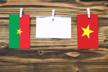 Hanging flags of Burkina Faso and Vietnam attached to rope with clothes pins with copy space on white note paper on wooden background.Diplomatic relations between countries.