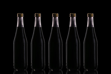 Five large glass bottles with a black drink stand on a mirror surface against a dark background in the center.