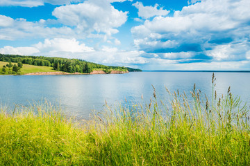 Fototapeta na wymiar Beautiful panoramic view of the Kama river from the hill in the foreground green grass, summer blue sky with clouds.