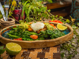 Tasty salad with egg, tomato, guacamole sauce, with crackers, lime and herbs on a craft plate