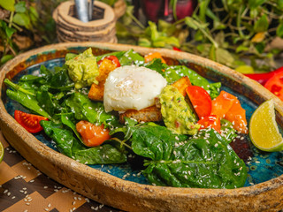 Tasty salad with egg, tomato, guacamole sauce, with crackers, lime and herbs on a craft plate