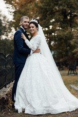 Fototapeta premium Wedding couple in autumn. Pretty bride and stylish groom. Amazing smiling wedding couple. A nice bride and groom in a luxury dress look at each other in a fairy forest. Lovers and happy people
