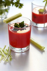 One glass with tomato juice and parsley decoration, a second glass with tomato juice and celery sprig.