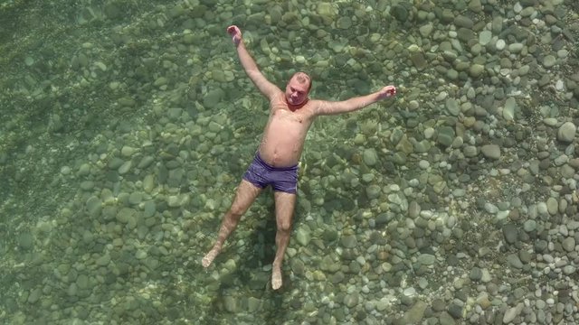 Adult man swims in sea in summer. man lies on surface of water on his back swinging on waves in sea. top view.