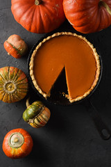 Traditional homemade pumpkin pie and bright squashes on black background top view copy space. Low key still life with natural lighting