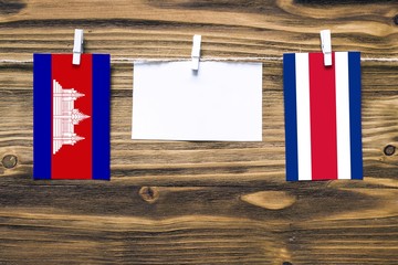 Hanging flags of Cambodia and Costa Rica attached to rope with clothes pins with copy space on white note paper on wooden background.Diplomatic relations between countries.