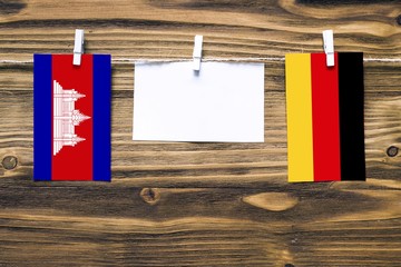 Hanging flags of Cambodia and Germany attached to rope with clothes pins with copy space on white note paper on wooden background.Diplomatic relations between countries.
