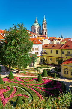 Green lawns and elaboratelz cut shrubs of Vrtba garden with roof of st. Nicholas church in Prague, Czech Republic, on a bright day with blue sky