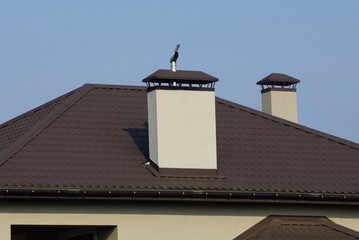 large chimney pipe on a brown tiled roof against a blue sky