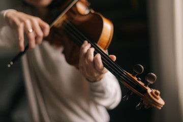 Handsome woman musician plays the violin in her home, close-up. Female 's face is not visible.