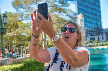 Happy woman with sunglasses visiting big city in the summer making selfies with smartphone