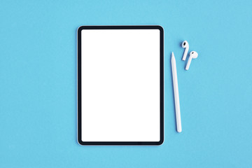 Tablet mockup with white pencil and wireless earphones on blue background. Top view. Copy space.