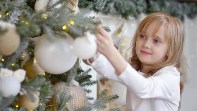 Close up of pretty little girl smiling and putting star on Christmas tree while decorating home for holiday