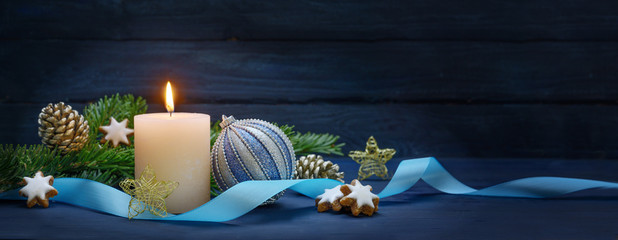 Burning candle, fir branches with cones and cinnamon stars, blue Christmas bauble and a ribbon, as...