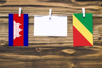 Hanging flags of Cambodia and Republic Of The Congo attached to rope with clothes pins with copy space on white note paper on wooden background.Diplomatic relations between countries.