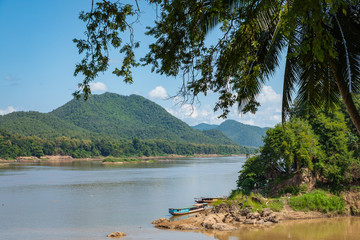 Traditional Long Boat on the Mekong River and mountains view in Luang Prabang, Laos.