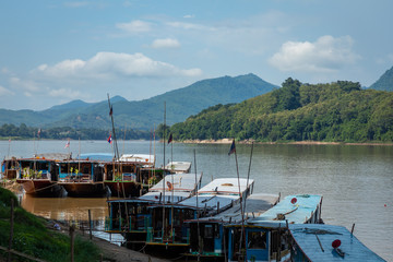 Traditional Long Boat on the Mekong River and mountains view in Luang Prabang, Laos.