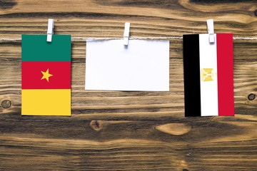 Hanging flags of Cameroon and Egypt attached to rope with clothes pins with copy space on white note paper on wooden background.Diplomatic relations between countries.